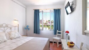 A bedroom with a bed, a chair, a table with fruit, a TV, and a window with curtains. - Hotel Caleta  (Lloret de Mar)