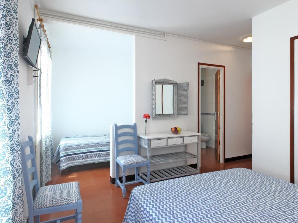 Une chambre avec deux lits, un bureau avec un miroir, une chaise et une petite table sur laquelle est posé un vase de fleurs.