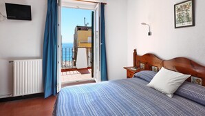 A bedroom with a bed, a nightstand, a TV, and a view of the sea. - Hotel Caleta  (Lloret de Mar)