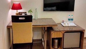 A compact hotel room with a single bed, a desk with a chair, a TV mounted on the wall, and a small trash bin. - Jb innovations (Lucknow)