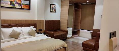 A modern hotel room with a large bed, a seating area, a wardrobe, and a painting on the wall.