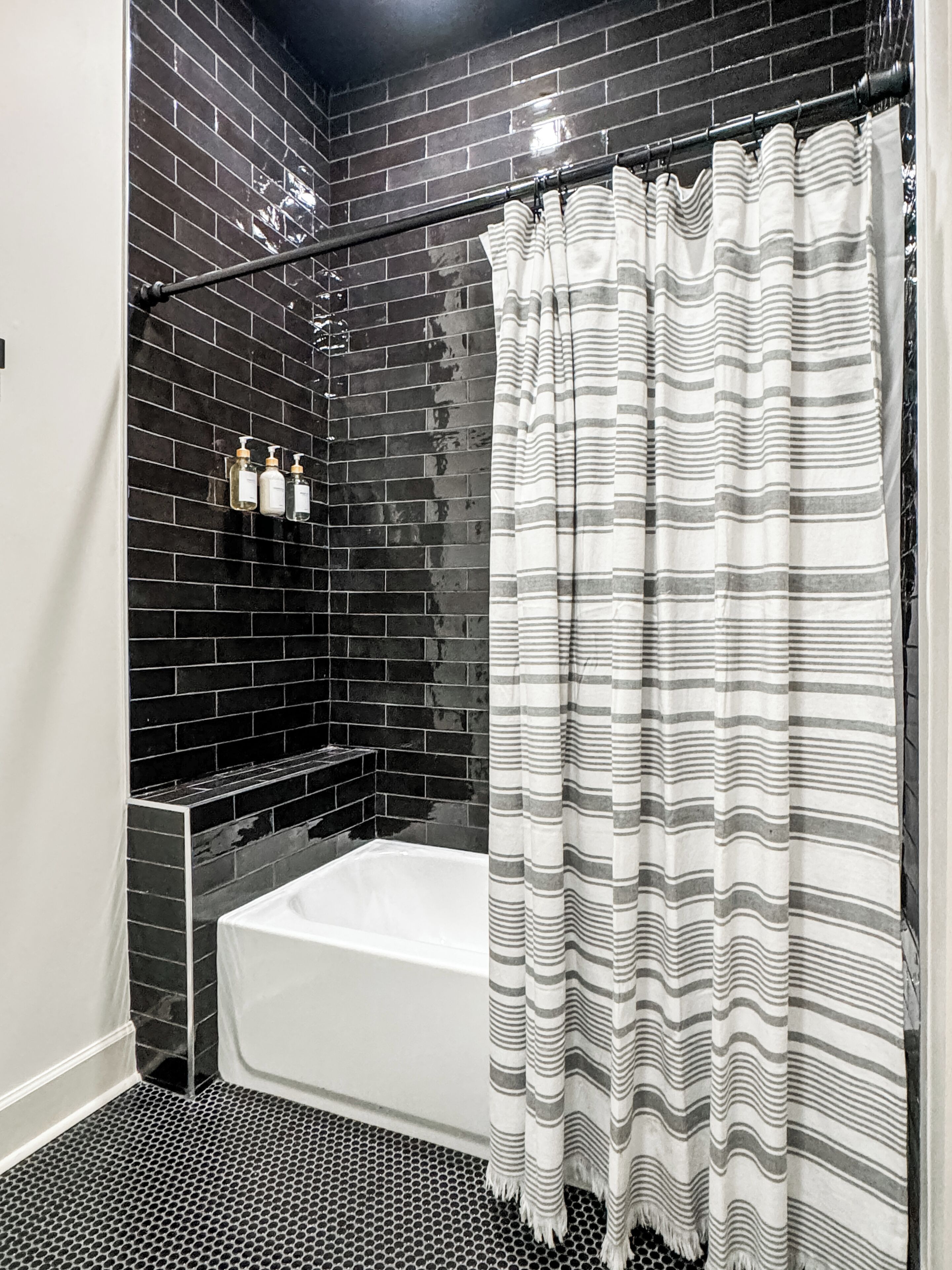 Un baño con pared de azulejos negros, una bañera blanca y una cortina de ducha a rayas.