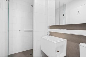 Een moderne badkamer met een douchecabine van glas, een wit wastafel en een meubel met een spiegel.