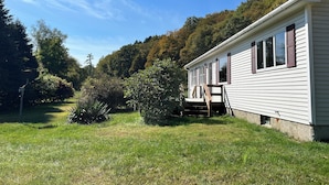 A single-story house with a front porch, surrounded by a grassy yard and dense trees. - Quiet Country 2 Bedroom Home Near Bellows Falls & Walpole — Easy I-91 Access (Westminster)