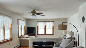 A living room with a sofa, a coffee table, a TV, and a ceiling fan. - Quiet Country 2 Bedroom Home Near Bellows Falls & Walpole — Easy I-91 Access (Westminster)