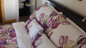 A bedroom with a bed featuring a floral duvet cover, a bedside table with a lamp, and a wall-mounted picture frame.