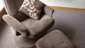 A living room with a brown armchair, a matching ottoman, a fireplace, and a framed picture on the wall.