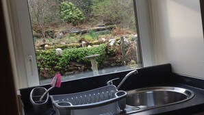A kitchen with a window view of a forested area, a sink, and a dish rack.