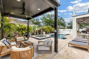 Un patio exterior cubierto con muebles de mimbre, una piscina y abundante vegetación.