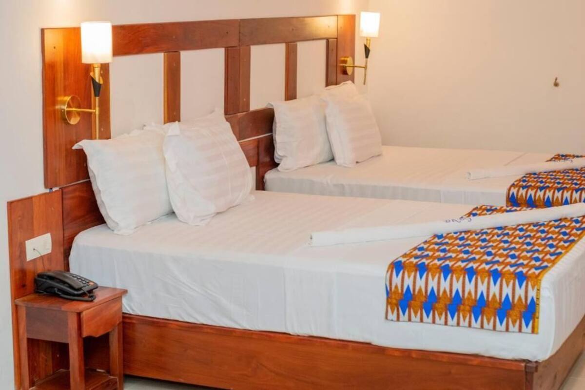 A hotel room with two beds, wooden headboards, white bedding, and a patterned throw blanket.