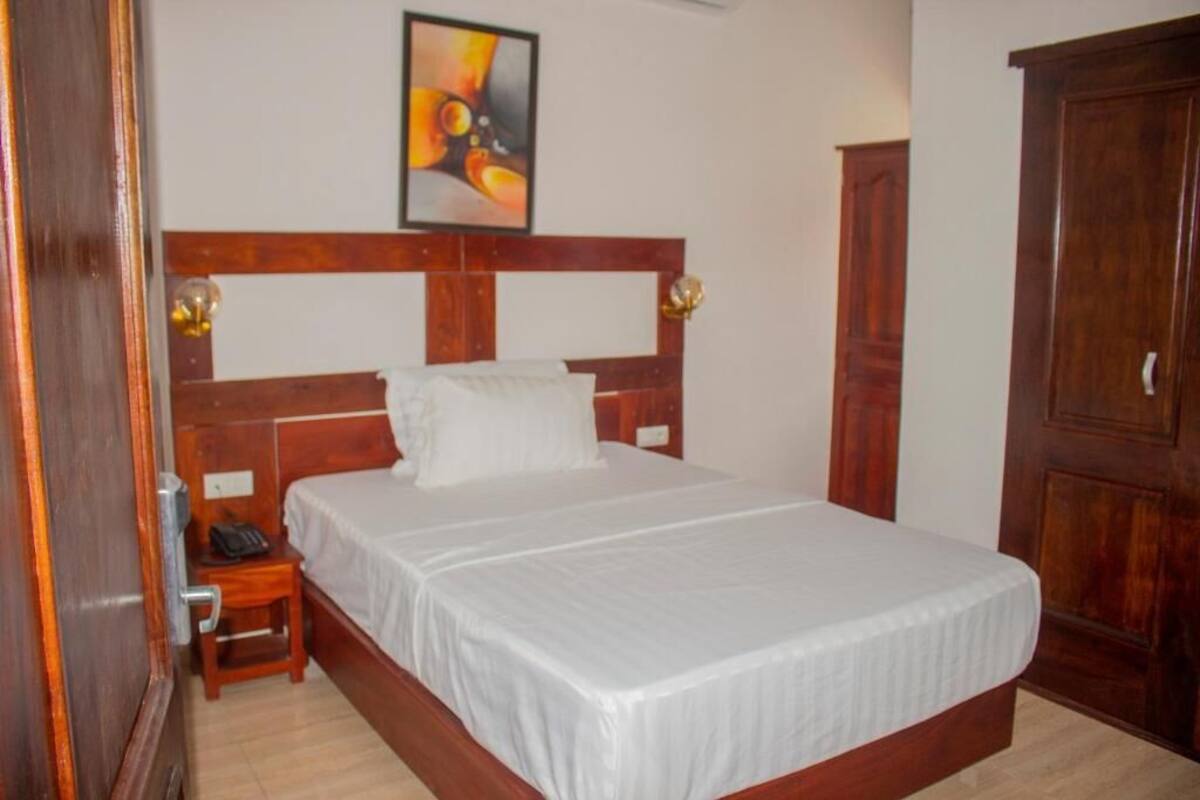 A bedroom with a wooden headboard, a white bedspread, a bedside table with a lamp, and a wardrobe.