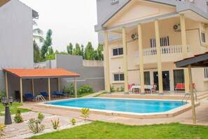 Um edifício de dois andares com piscina, área de estar ao ar livre e um pátio coberto.