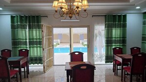 A dining area with a pool view, a chandelier, and green curtains.
