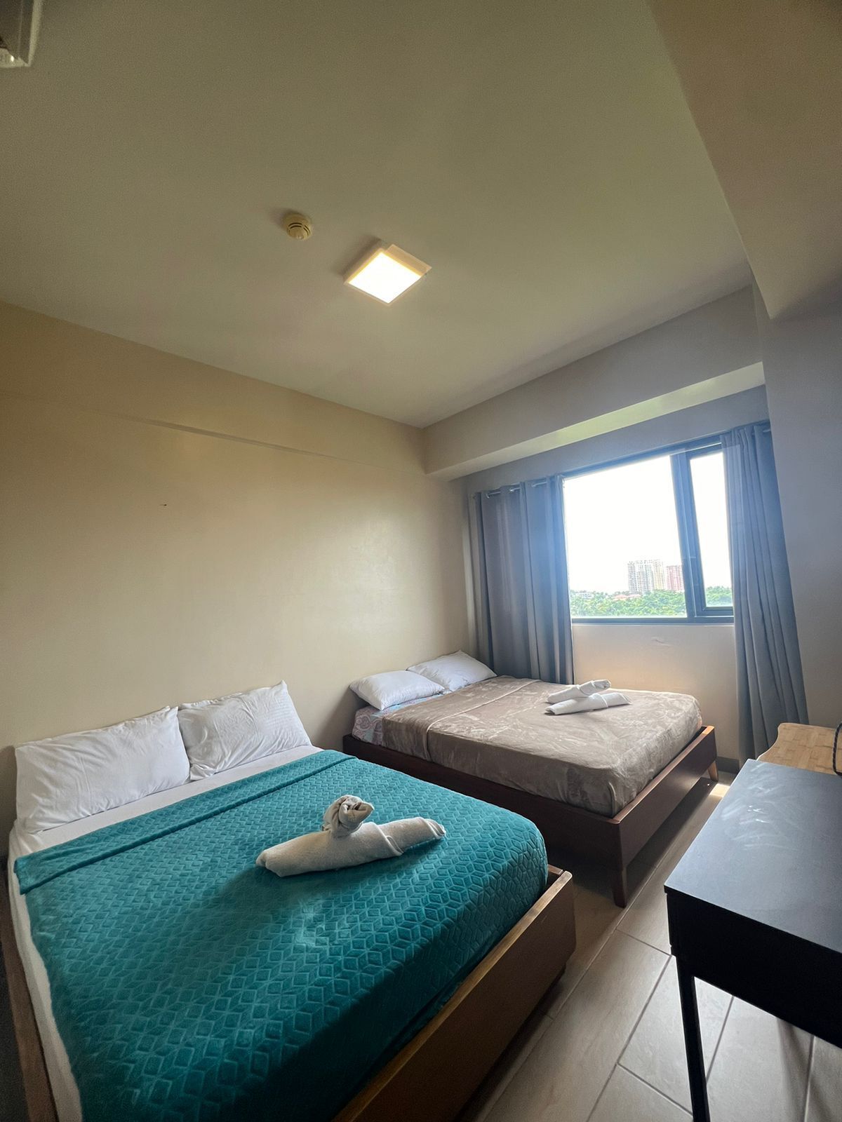 Hotellihuone, jossa on kaksi sänkyä, työpöytä ja ikkuna, jossa on verhot.