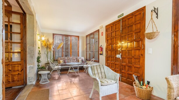Un interior acogedor con puerta de madera, muebles de mimbre, un sofá y suelo de baldosas.