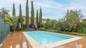 Una piscina rectangular con borde de azulejos, rodeada por un muro de ladrillo y altas cigarreras.