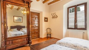 Una habitación con una cama de madera, un espejo, una silla y una ventana con cortinas.