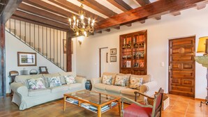 Una sala de estar con una escalera, una mesa de centro de vidrio, un sillón tapizado rojo y una estantería de madera.