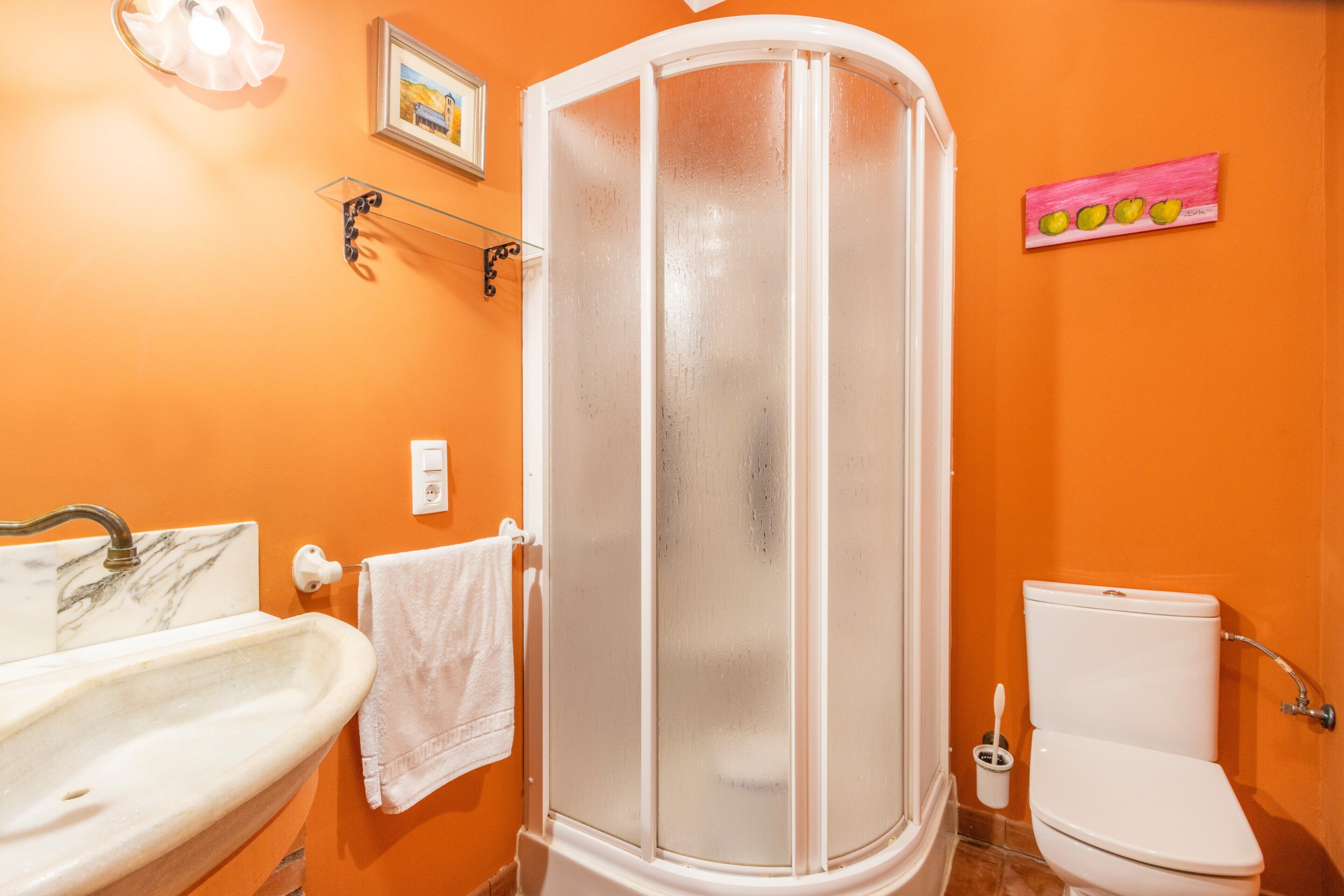 A bathroom with an orange wall, a white sink, a white toilet, and a glass shower enclosure.