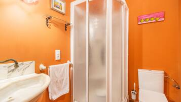 A bathroom with an orange wall, a white sink, a white toilet, and a glass shower enclosure.