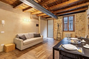 A cozy room with a wooden ceiling, a stone wall, a sofa, a dining table set with plates, glasses, and cutlery.
