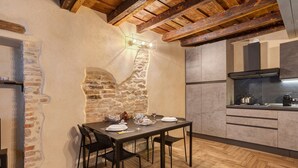 A dining area with a stone wall, wooden ceiling beams, a kitchen with modern appliances, and a herringbone wood floor. - Apartment 'Maison Le Chic' with Wi-Fi (Bergamo)