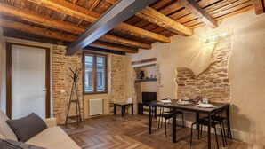 A cozy room with a stone wall, wooden beams, a fireplace, a dining table with chairs, and a sofa. - Apartment 'Maison Le Chic' with Wi-Fi (Bergamo)