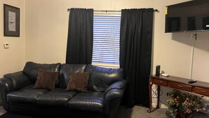 A living room with a black leather sofa, a wooden side table, and a television mounted on the wall.