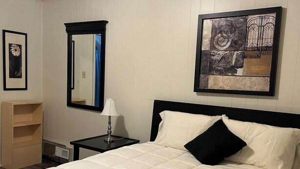 A neatly made bed with a black headboard, a bedside table with a lamp, and a framed picture on the wall.