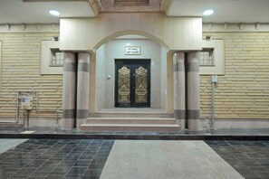 Entrada de un edificio con puertas dobles, un cartel encima y suelo de baldosas.