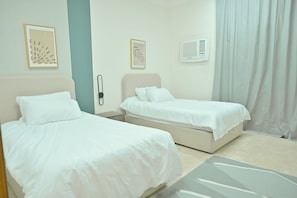 Een hotelkamer met twee bedden, een nachtkastje, een aan de muur bevestigd telefoontoestel en een raam met gordijnen.