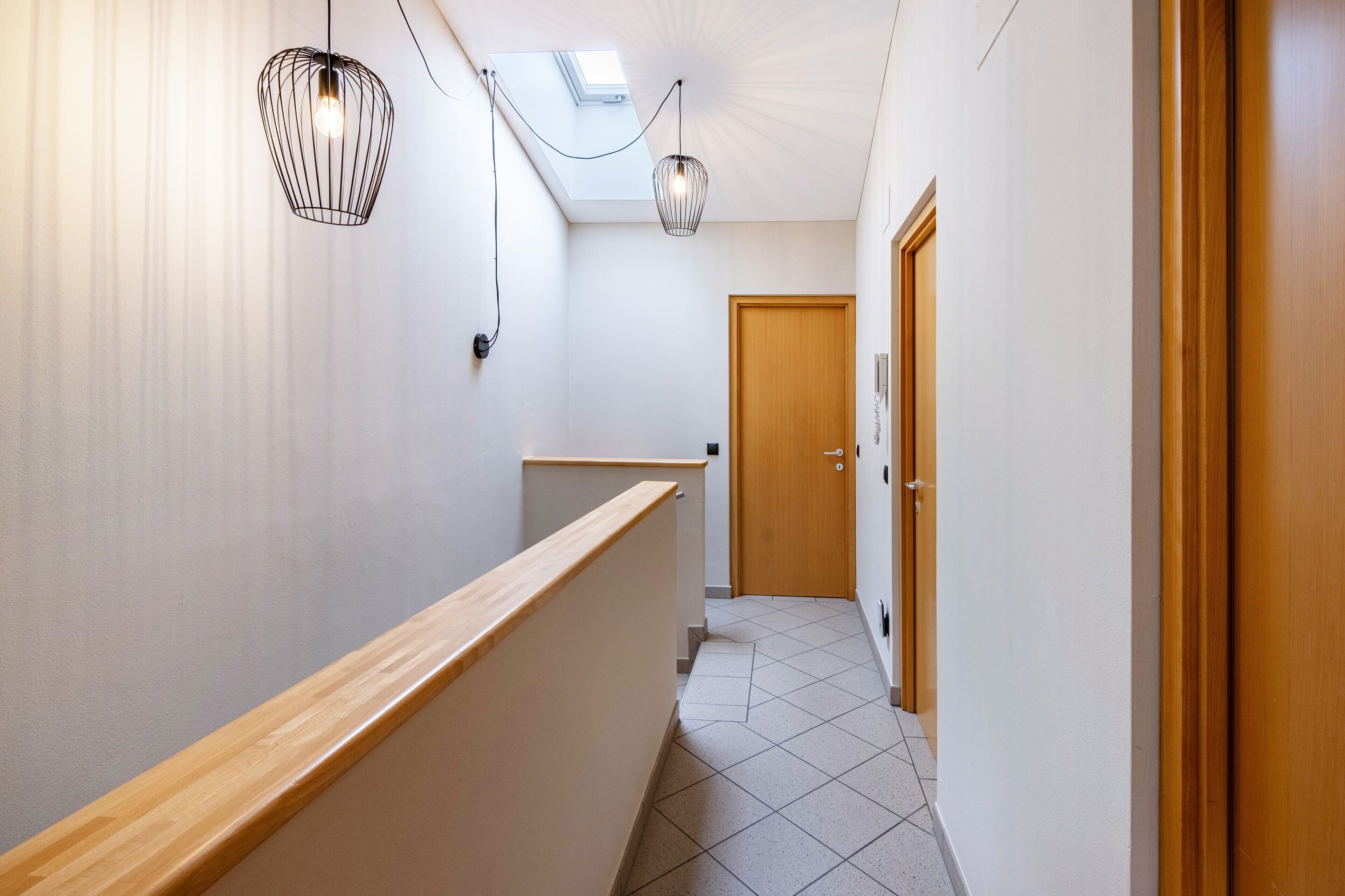 A hallway with a wooden handrail, a skylight, and a door at the end.