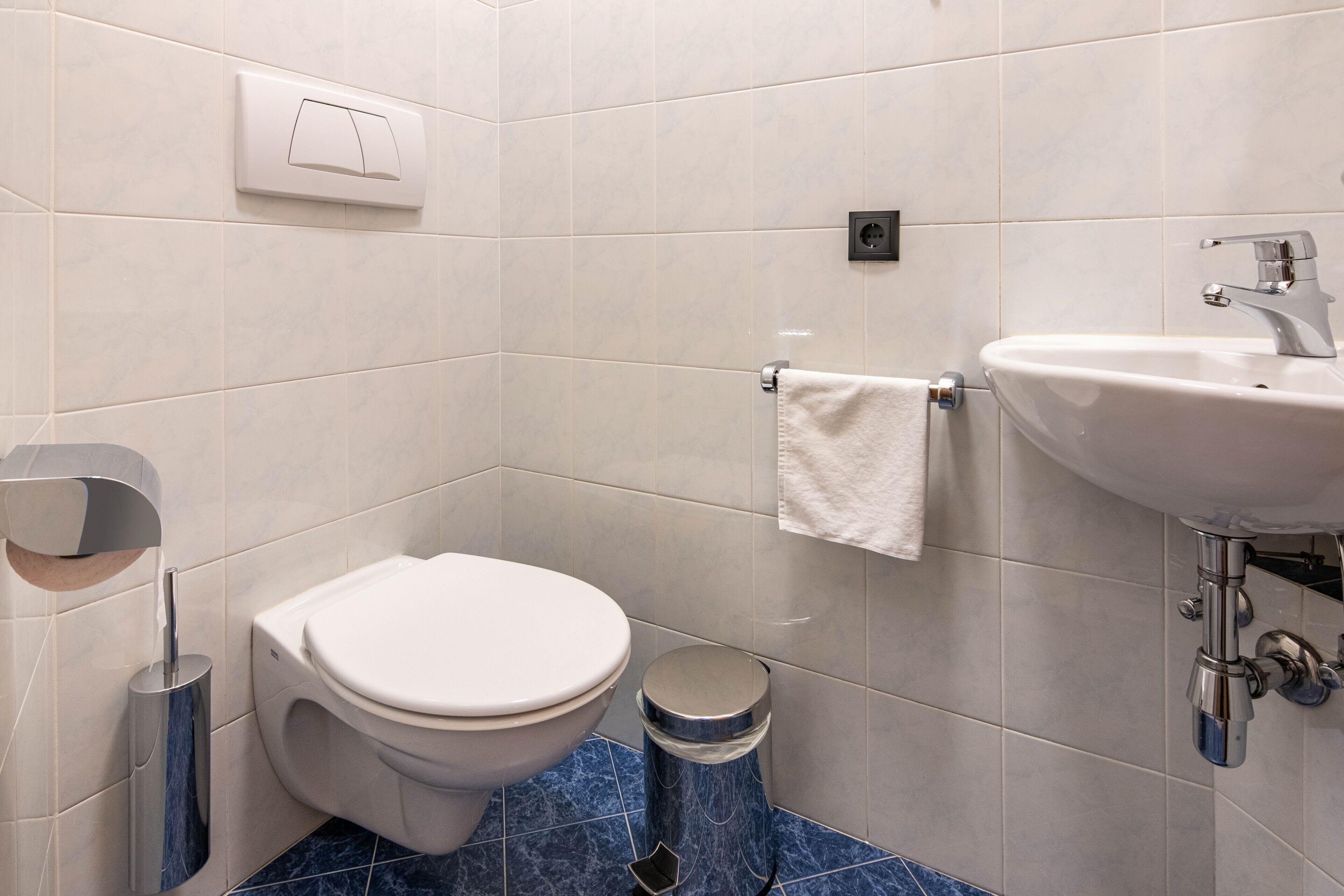 A modern bathroom with a toilet, sink, and trash bin.