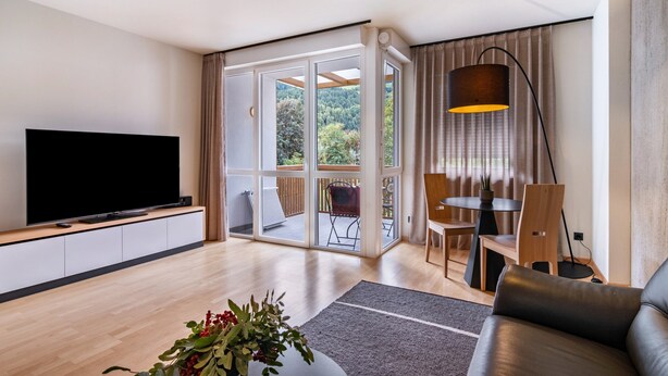 Un salón moderno con un televisor de pantalla plana, un sofá, una mesa de comedor con sillas y un ventanal con vistas a zonas verdes.