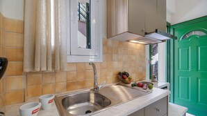 A kitchen with a stainless steel sink, a window with curtains, and a green door.