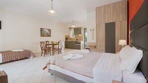 A hotel room with a bed, a desk, a chair, a small kitchen area, and a bathroom.