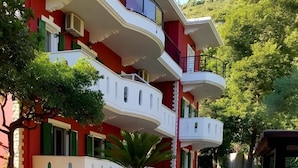 A multi-story building with balconies, a potted plant, and purple flowers in the foreground.