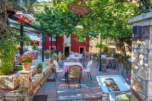 Un café al aire libre con paredes de piedra, plantas en macetas y mesas con sillas.