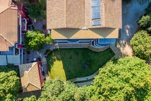 Luchtbeeld van een woonhuis met een groot gazon, een stenen pad en een gebouw met een rood dak.