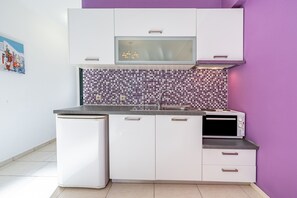 Une cuisine compacte avec des meubles blancs, un pare-feu en carrelage, un four à micro-ondes encastré et un évier.