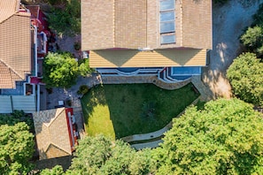 Vista aérea de uma propriedade residencial com um extenso gramado, um caminho de pedra e uma construção com telhado vermelho.