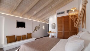 A bedroom with a large bed, a TV mounted on the wall, a wooden ceiling, and a bench with cushions. - Room 'Deluxe Loft - B' with Shared Terrace, Wi-Fi and Air Conditioning (Parga)