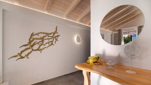 A modern interior with a wooden ceiling, a wall-mounted abstract gold art piece, a round mirror, a wooden table with a glass of juice, and a decorative item. - Room 'Deluxe Loft - B' with Shared Terrace, Wi-Fi and Air Conditioning (Parga)