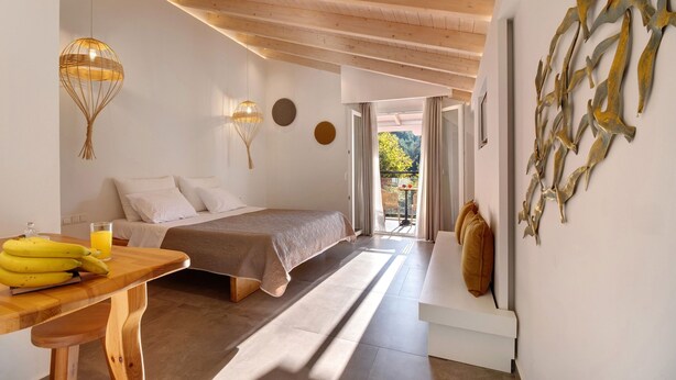 A bedroom with a bed, bedside table with bananas and a glass of orange juice, a wooden ceiling, and a view through an open door. - Room 'Deluxe Loft - B' with Shared Terrace, Wi-Fi and Air Conditioning (Parga)