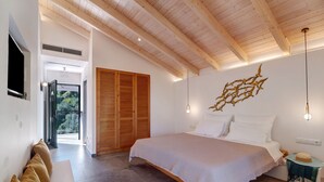 Quarto com cama, vigas de madeira no teto, luminária na parede e vista por uma porta aberta.