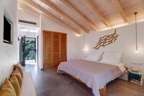Een slaapkamer met een bed, houten balken in het plafond, een wandlamp en uitzicht door een open deur.