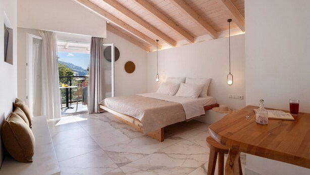 A bedroom with a bed, a wooden table, a balcony with a view, and a ceiling with wooden beams. - Room 'Deluxe Loft - D' with Shared Terrace, Wi-Fi and Air Conditioning (Parga)