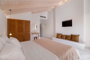 Een slaapkamer met een bed, een houten garderobe, een witte bank met kussens, een aan de muur bevestigde televisie en een hanglamp.