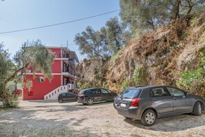 A building with a red facade, a staircase, and parked cars. - Room 'Deluxe Loft - D' with Shared Terrace, Wi-Fi and Air Conditioning (Parga)