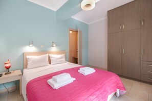 A bedroom with a bed, bedside lamps, a desk, a wardrobe, and a door to another room.